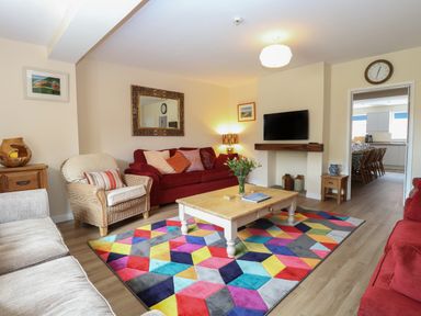 A living room with red sofas a wicker chair a wooden coffee table and a colorful geometric rug at Beach House in Winterton-On-Sea