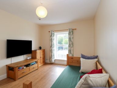 A small living room with a wall-mounted television wooden furniture and a daybed with cushions at Beach House in Winterton-On-Sea