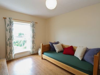 A room with a wooden daybed with cushions and a window with patterned curtains at Beach House in Winterton-On-Sea
