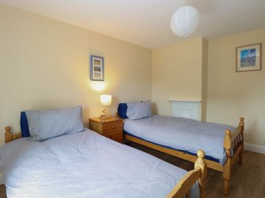 A bedroom with two single wooden beds a wooden bedside table with a lamp and framed pictures on the beige walls at Beach House in Winterton-On-Sea