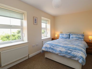 A bedroom with a bed with blue and white bedding two windows and two bedside tables with lamps at Beach House Winterton-On-Sea