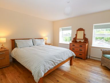 A bedroom with a wooden bed with striped bedding two bedside tables with lamps a wooden dresser with mirror and two windows at Beach House in Winterton-On-Sea
