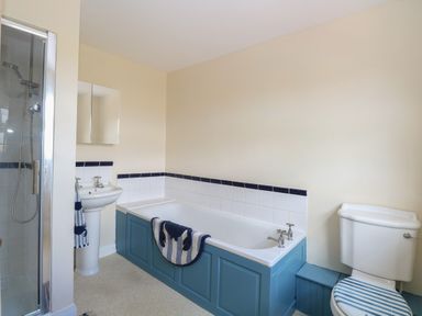 A bathroom with a shower cubicle a pedestal sink a bathtub with a blue panel and towel and a toilet with a striped seat cover at Beach House in Winterton-On-Sea