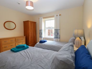 A bedroom with two single beds a wooden wardrobe and dresser a window with curtains and a lamp on a nightstand at Beach House in Winterton-On-Sea