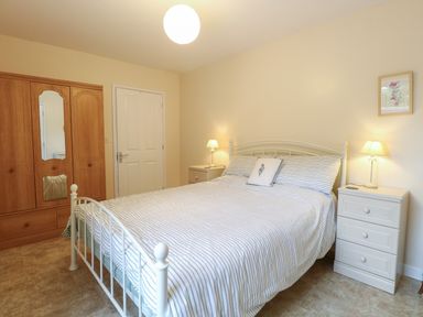 A bedroom with a double bed striped bedding two bedside tables with lamps wooden wardrobe and a closed door at Beach House in Winterton-On-Sea