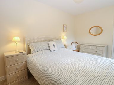 A bedroom with a bed striped bedding two bedside tables with lamps a chair a chest of drawers and an oval mirror at Beach House in Winterton-On-Sea