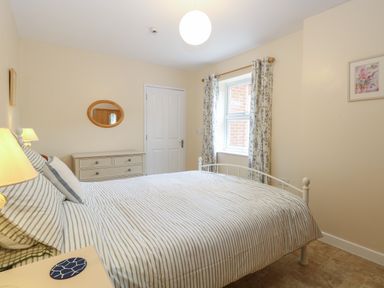 A bedroom with a bed a window with curtains a dresser and a door at Beach House in Winterton-On-Sea