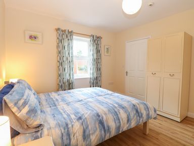 A bedroom with a double bed covered in blue and white bedding next to a window with patterned curtains and a cream wardrobe Beach House Winterton-On-Sea