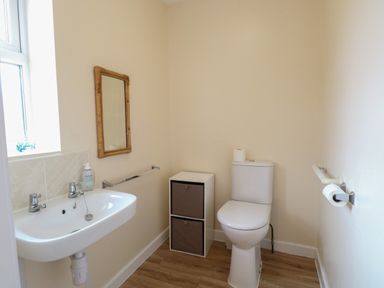A bathroom with a sink a mirror a toilet and storage unit at Beach House in Winterton-On-Sea