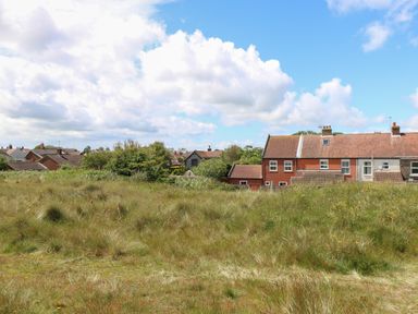 A grassy field with houses and trees in the background at Beach House in Winterton-On-Sea