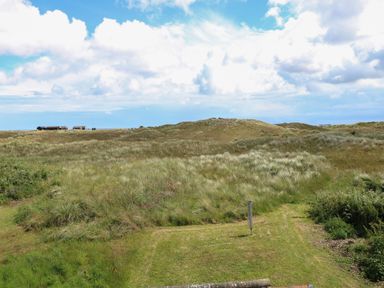 A grassy landscape with bushes and small hills under a partly cloudy sky at Beach House in Winterton-On-Sea