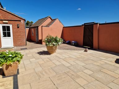 A patio area with stone tiles and potted plants next to a brick building and a peach-colored wall with a wooden gate at Beach House in Winterton-On-Sea