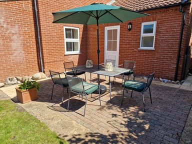 A brick patio with a glass table six chairs and a green umbrella at Beach House in Winterton-On-Sea