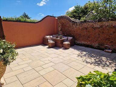 An outdoor patio with wicker furniture and cushions next to brick and orange walls with plants at Beach House in Winterton-On-Sea
