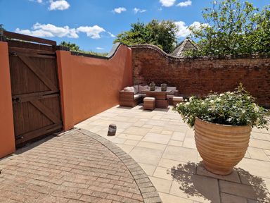 An outdoor patio with a wooden gate orange walls a wicker seating set and a large potted plant at Beach House Winterton-On-Sea