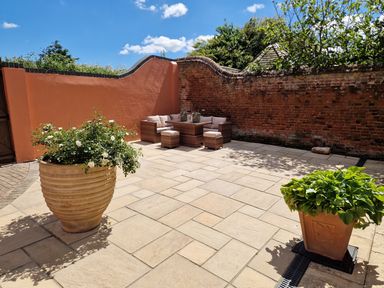 A paved outdoor patio with potted plants and wicker seating against a brick and plaster wall at Beach House in Winterton-On-Sea