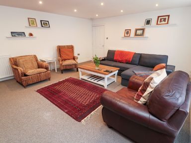 A living room with two wicker chairs a leather armchair a gray sofa a wooden coffee table and a red rug at The Old Factory House in Berwick-Upon-Tweed