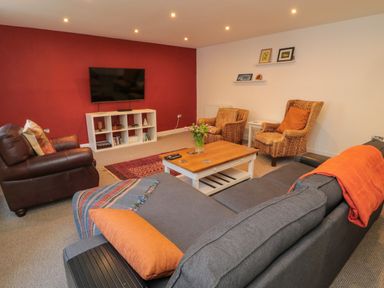 A living room with a gray sofa and orange pillows a wooden coffee table and a television on a red wall at The Old Factory House in Berwick-Upon-Tweed