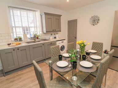 A kitchen with grey cabinets a glass dining table set for six with black mugs and white bowls at The Old Factory House in Berwick-Upon-Tweed
