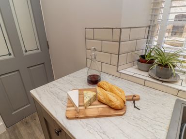A kitchen countertop with cheese bread a glass bottle with liquid and two potted plants near a window at The Old Factory House in Berwick-Upon-Tweed