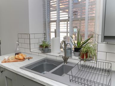 A kitchen sink with plants on the windowsill and a cutting board with bread cheese and a bottle at The Old Factory House in Berwick-Upon-Tweed