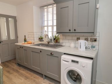 A kitchen with gray cabinets a double sink a washing machine a kettle and two potted plants on windowsill at The Old Factory House in Berwick-Upon-Tweed