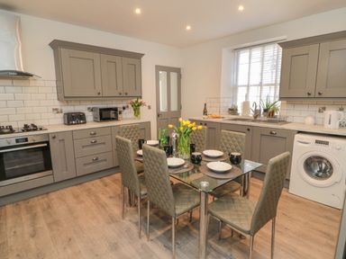 A kitchen with grey cabinets a glass dining table with six chairs and yellow flowers at The Old Factory House in Berwick-Upon-Tweed