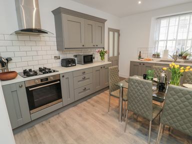 A kitchen with grey cabinets a glass dining table and chairs and flowers on the table at The Old Factory House in Berwick-Upon-Tweed