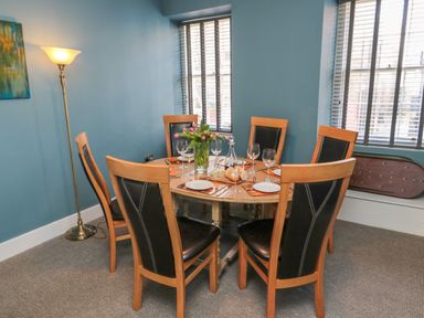 A dining room with a round wooden table set for six people and a floor lamp at The Old Factory House in Berwick-Upon-Tweed