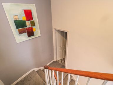 A staircase with carpeted steps and a wooden handrail leading to a closed door at The Old Factory House in Berwick-Upon-Tweed