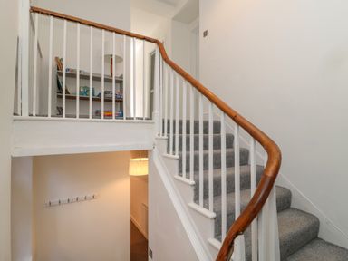 A staircase with gray carpet and a wooden handrail leading to a hallway with shelves and a lamp at The Old Factory House in Berwick-Upon-Tweed