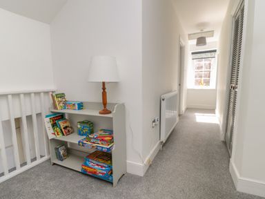 A hallway with a bookshelf holding books and board games and a lamp near a window and radiator at The Old Factory House in Berwick-Upon-Tweed