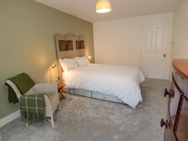 A bedroom with a bed a chair with blankets a wooden dresser and a door at The Old Factory House in Berwick-Upon-Tweed
