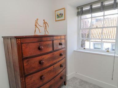 A wooden chest of drawers with two wooden mannequin figures on top next to a window with blinds at The Old Factory House in Berwick-Upon-Tweed