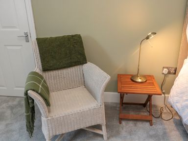 A wicker chair with green blankets next to a wooden side table with a lamp at The Old Factory House in Berwick-Upon-Tweed