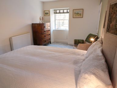 A bedroom with a bed a wooden chest of drawers a wicker chair and two framed pictures on the wall at The Old Factory House in Berwick-Upon-Tweed