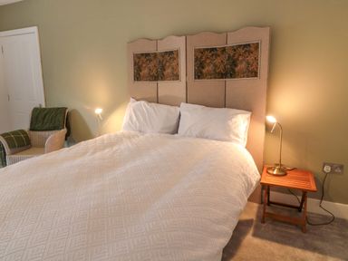 A bedroom with a bed a headboard two pillows bed side table with lamp and armchair at The Old Factory House in Berwick-Upon-Tweed