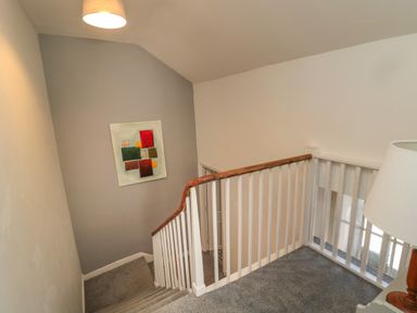 A stairway with carpeted steps and a wooden handrail with white balusters and a painting on a grey wall at The Old Factory House in Berwick-Upon-Tweed