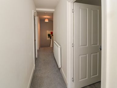 A hallway with carpet flooring a radiator and an open door at The Old Factory House in Berwick-Upon-Tweed