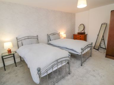 A bedroom with two single beds a glass bedside table with a lamp a wooden chest of drawers a round mirror a standing mirror and a wardrobe at The Old Factory House in Berwick-Upon-Tweed