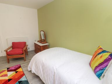 A bedroom with a white bedspread and colorful pillow a wooden chair with red cushions and a small dresser with a mirror at The Old Factory House in Berwick-Upon-Tweed