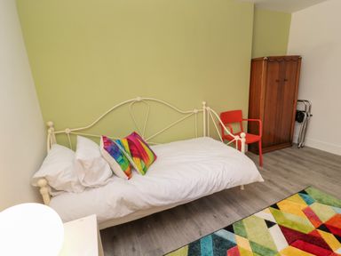 A bedroom with a white metal bed frame colorful pillows a red chair a wooden wardrobe and a multicolored rug at The Old Factory House in Berwick-Upon-Tweed