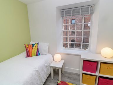 A bedroom with a single bed with a colorful pillow a small table with a spherical lamp a window with blinds and a storage unit with colorful drawers at The Old Factory House in Berwick-Upon-Tweed