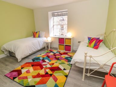 A bedroom with two beds a colorful rug and storage boxes under a window at The Old Factory House in Berwick-Upon-Tweed