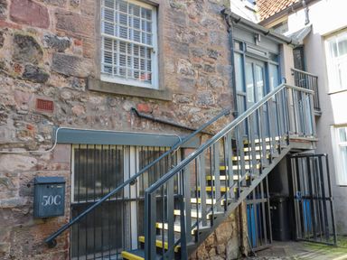 An outdoor staircase with metal railing leading to a blue door on a stone building at The Old Factory House in Berwick-Upon-Tweed