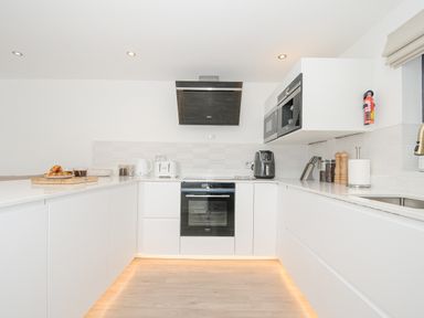 A kitchen with white cabinets appliances and a countertop with bread and kitchen utensils at 100 Hillside Villas in Looe