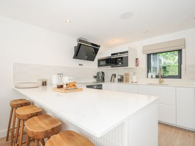 A kitchen with a white island countertop and wooden stools white cabinets and black appliances at 100 Hillside Villas in Looe