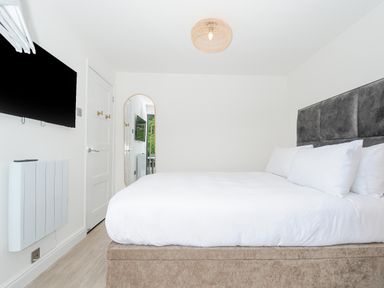 A bedroom with a bed with white linens a wall mounted television a door and a full length mirror at 100 Hillside Villas in Looe