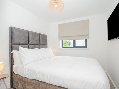 A bedroom with a double bed a bedside table with a lamp a window with a blind and a wall-mounted television at 100 Hillside Villas in Looe