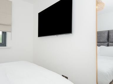 A bedroom with a mounted flat screen TV on a white wall and a bed with white bedding at 100 Hillside Villas in Looe